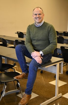 A man in a green sweater sitting on a table