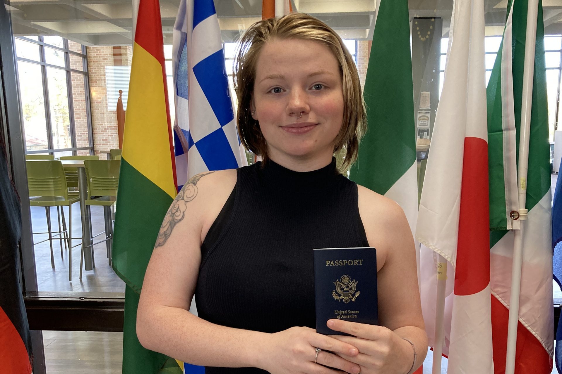 Photo of Kiersten Bible holding a passport with flags behind her.