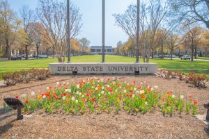 Flowers in front of Delta State campus quadrangle entry sign.