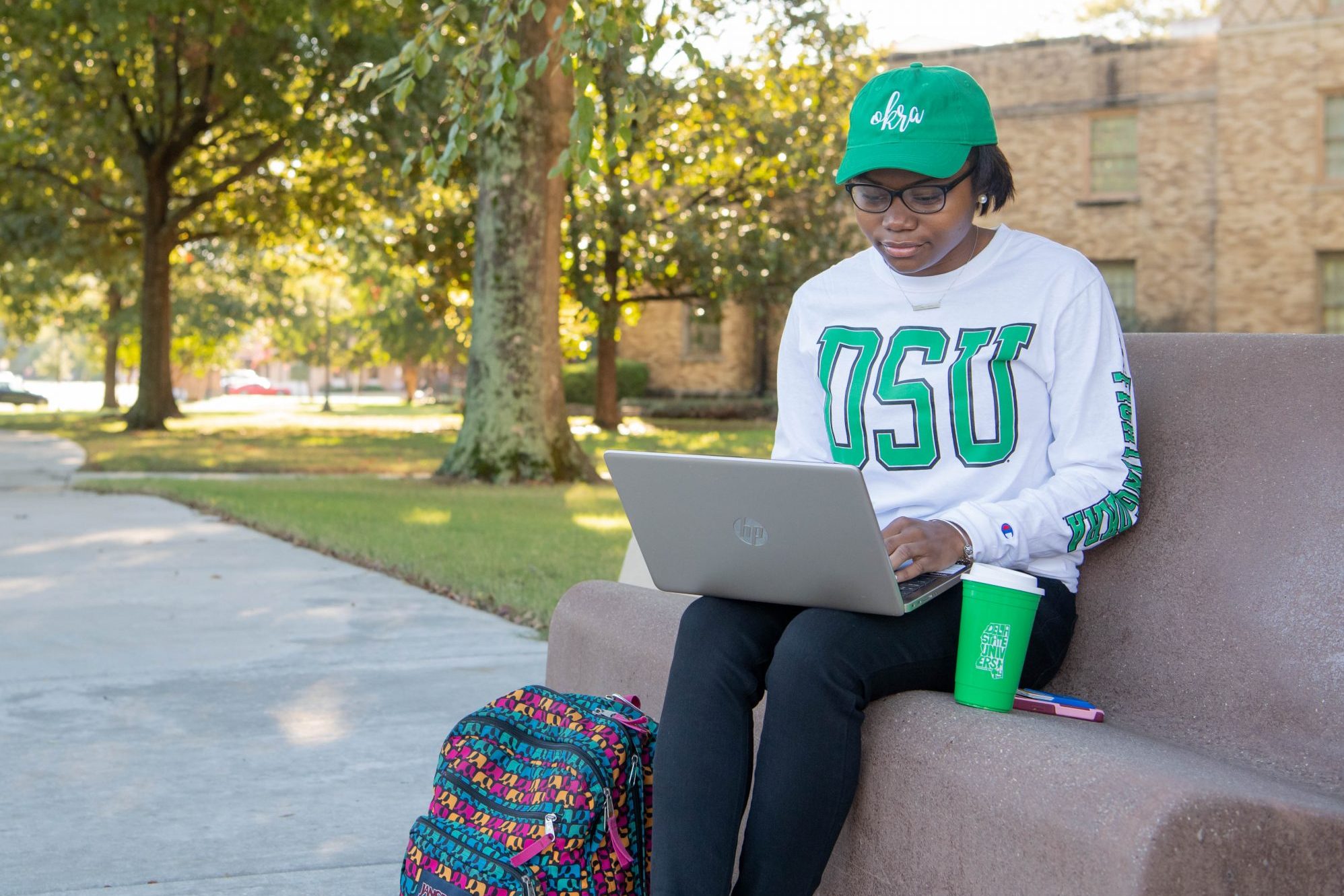 Student sitting outside on campus looking at laptop for scholarship information.