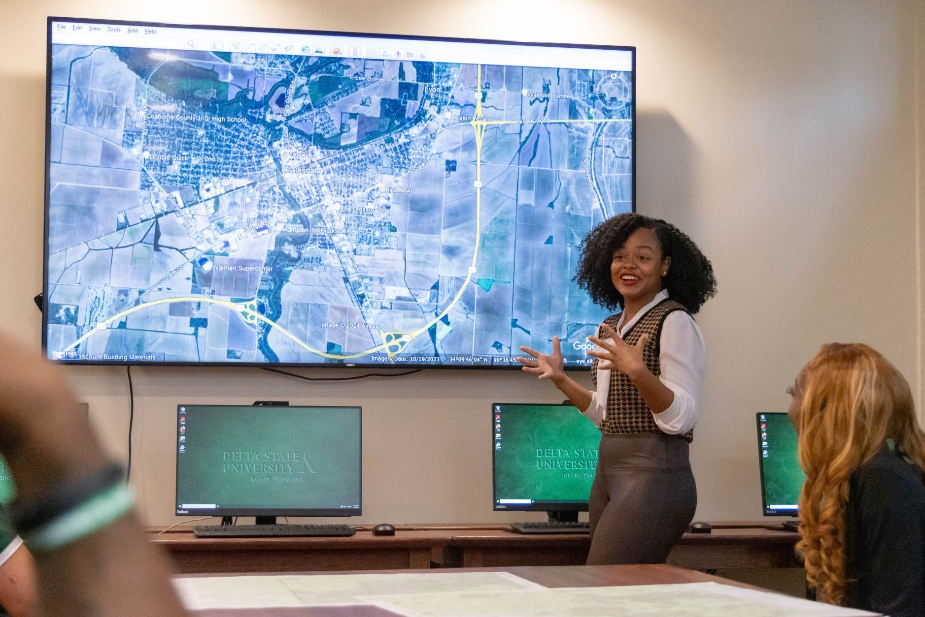 Student leading a class discussion using a large digital map display in a computer lab.