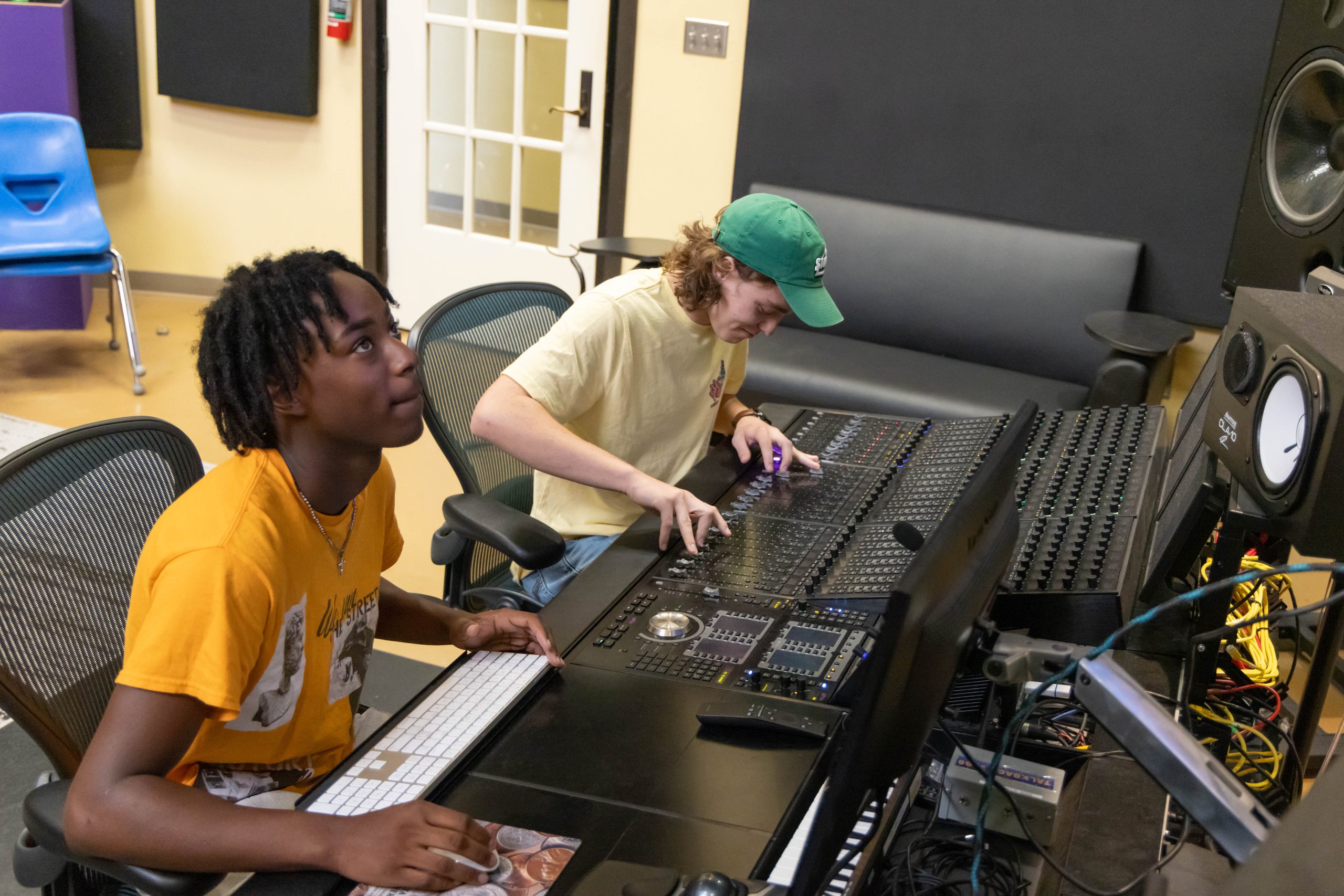Students working at a professional audio mixing console in a recording studio during a hands-on production session.