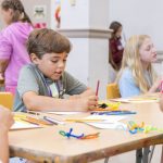 a young boy sitting at a desk doing arts and crafts